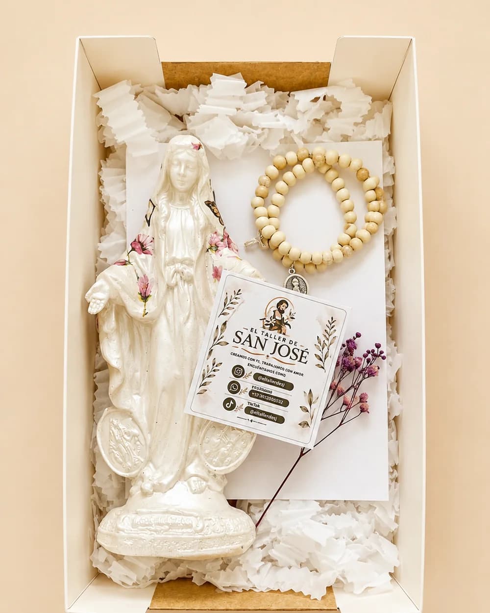 Caja abierta con una figura de la Sagrada Familia, un rosario y una tarjeta de El Taller de San José